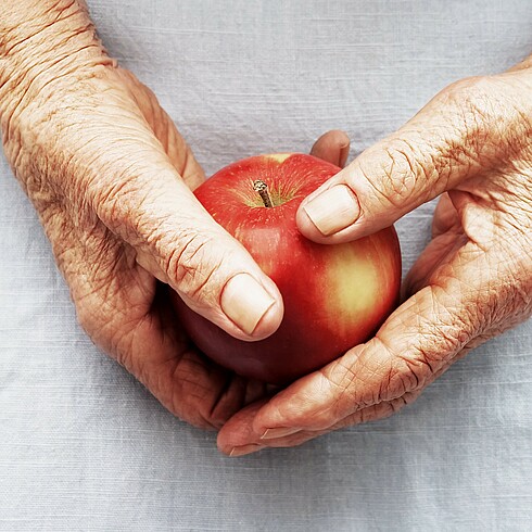 Die Hände einer älteren Person halten einen roten Apfel.